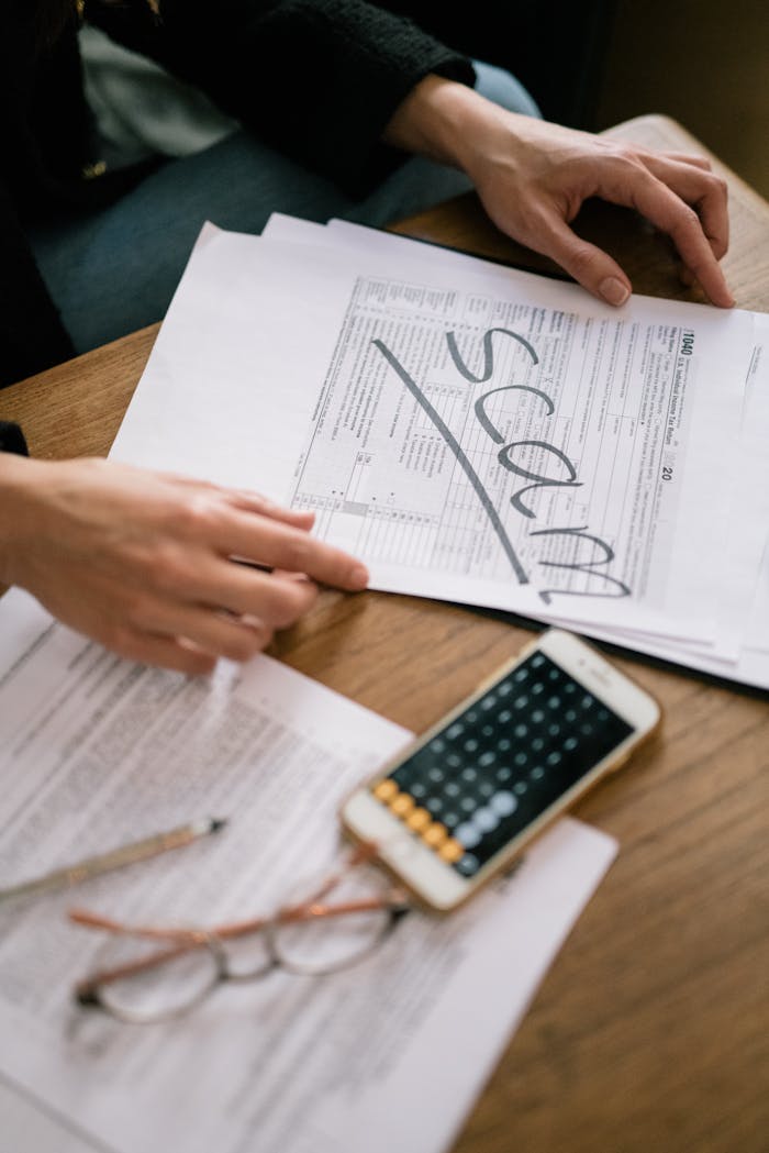 Close-up of hands examining documents marked scam with a calculator nearby.